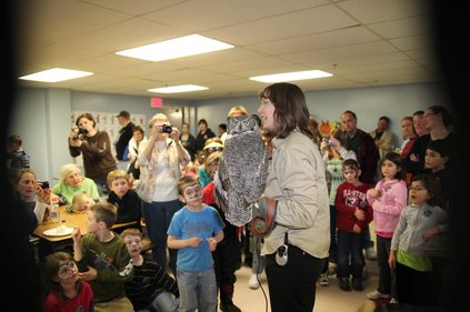 Karla holds Alice the great horned owl at the first owl festival, as children and adults crowd around.