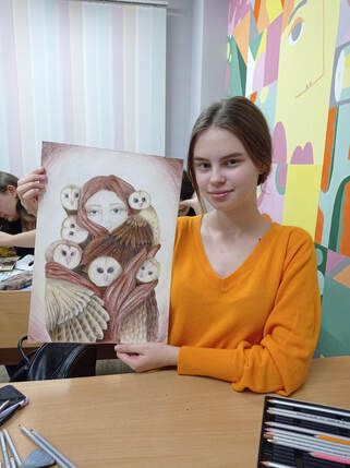 A teenage Ukrainian girl holding up her owl art.