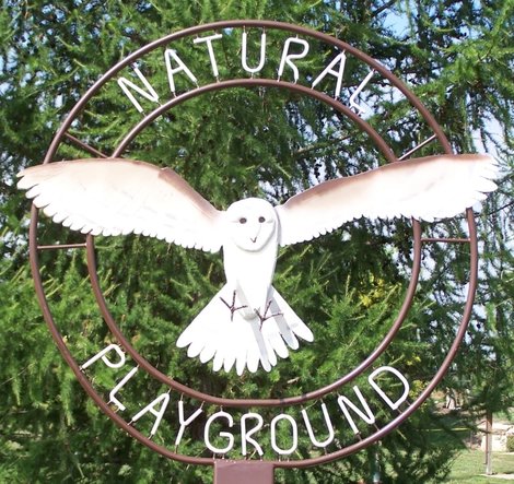 Photo of the natural playground welcome sign: a metal barn owl with spread wings on top of a circle
